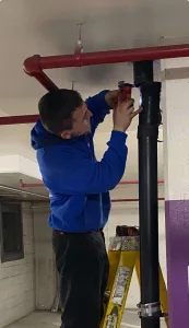 A Madden employee on a ladder working on a piece of pipe
