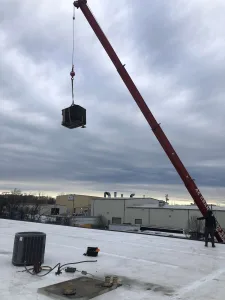 A crane lifting an exterior HVAC unit onto a roof
